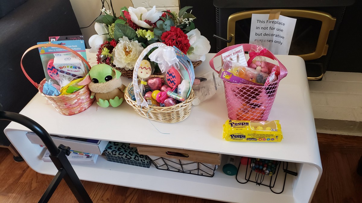A collection of gift baskets filled with candy and a stuffed toy, placed on a decorated shelf next to floral arrangements.