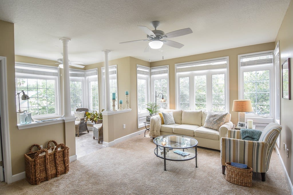 A bright and spacious living room with large windows, featuring a comfortable sofa, coffee table, and a ceiling fan.