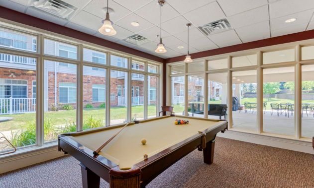 A well-lit recreation room with a pool table and large windows.