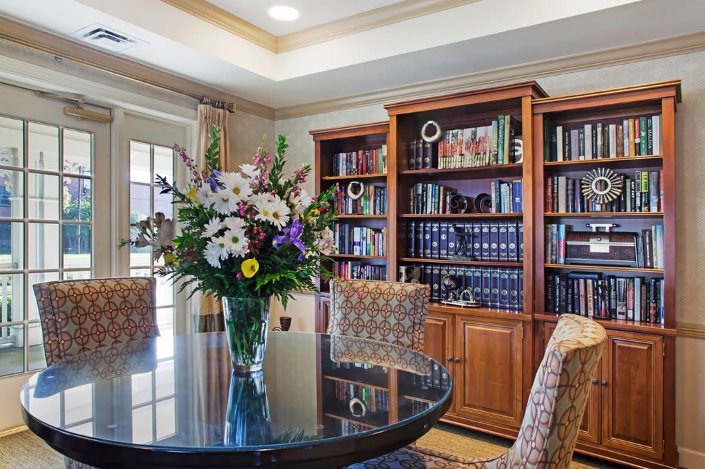 A cozy library with a round table, floral arrangement, and bookshelves filled with books.