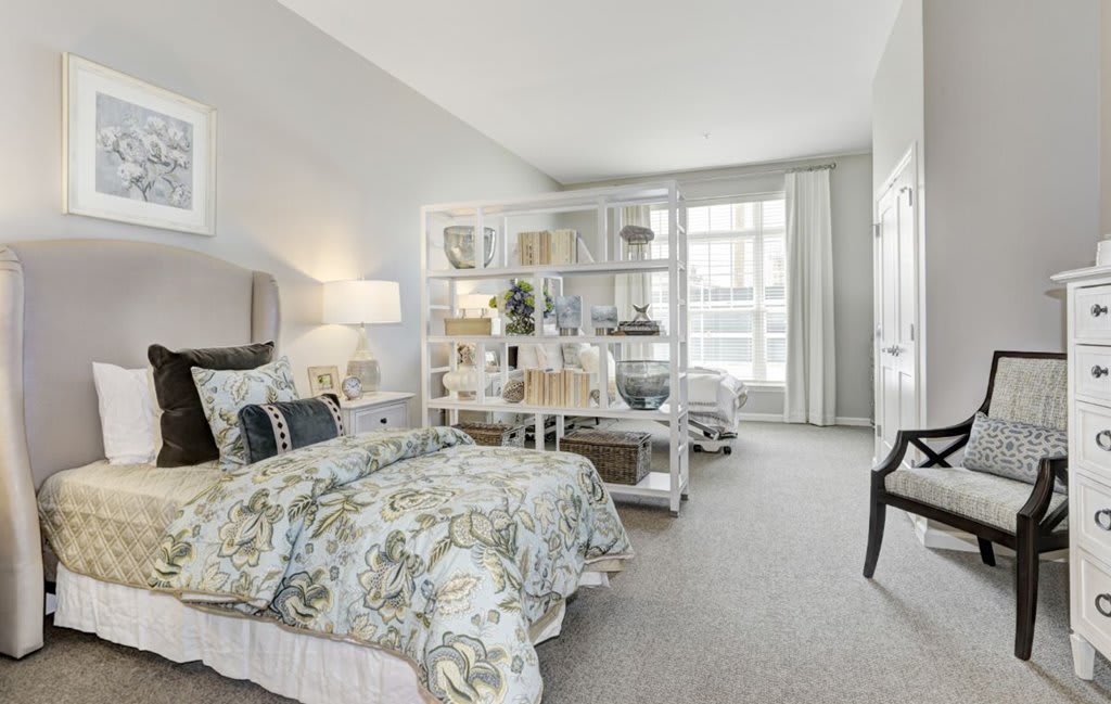 A stylish and cozy bedroom with a decorative bookshelf, ample natural light, and elegant furnishings.