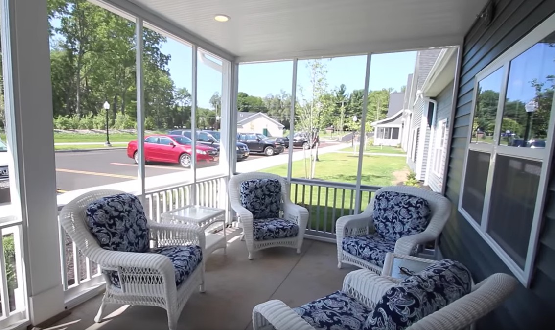 A cozy screened porch with wicker furniture overlooking a residential street.