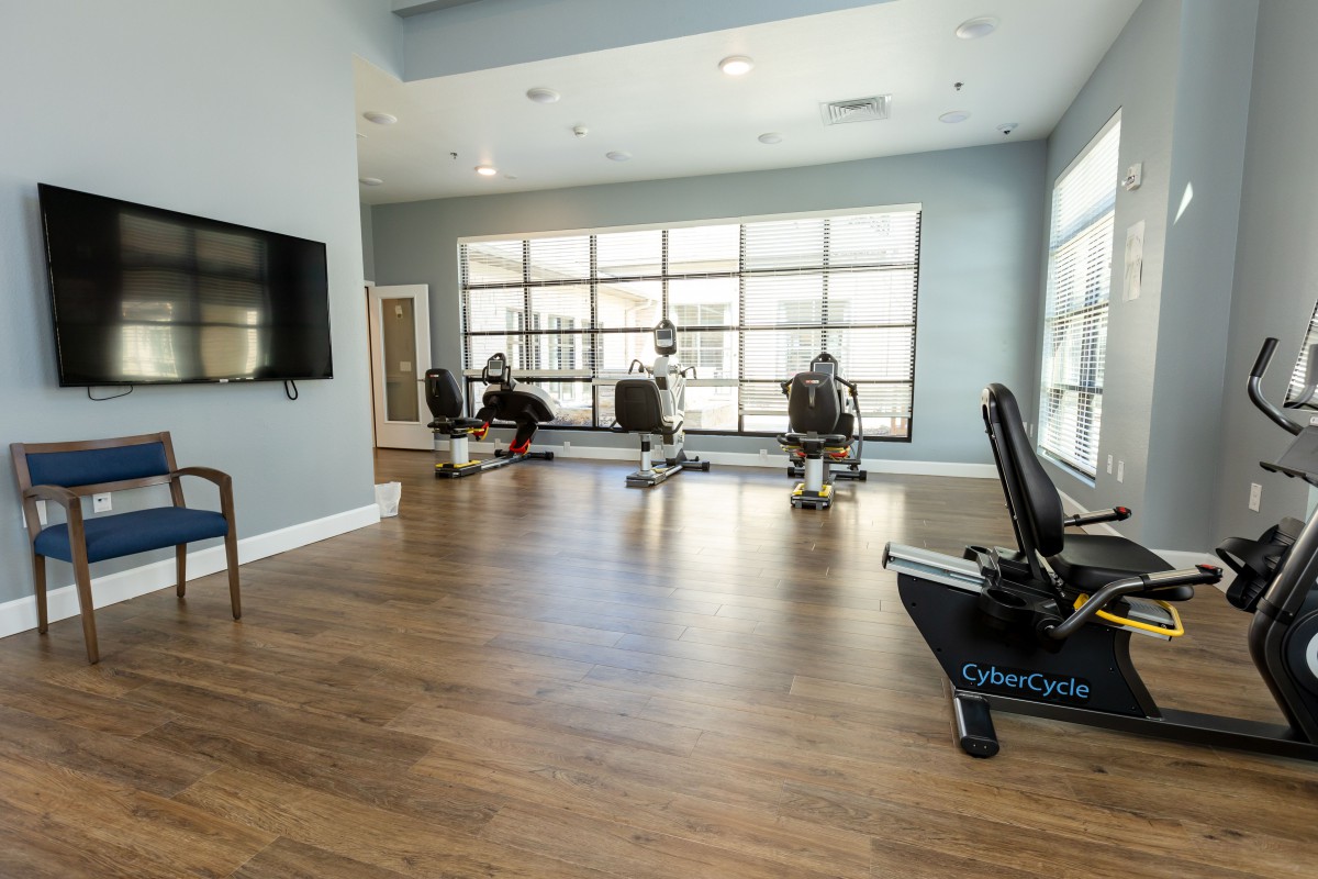 A modern gym with exercise equipment and a wooden floor, designed for workouts.