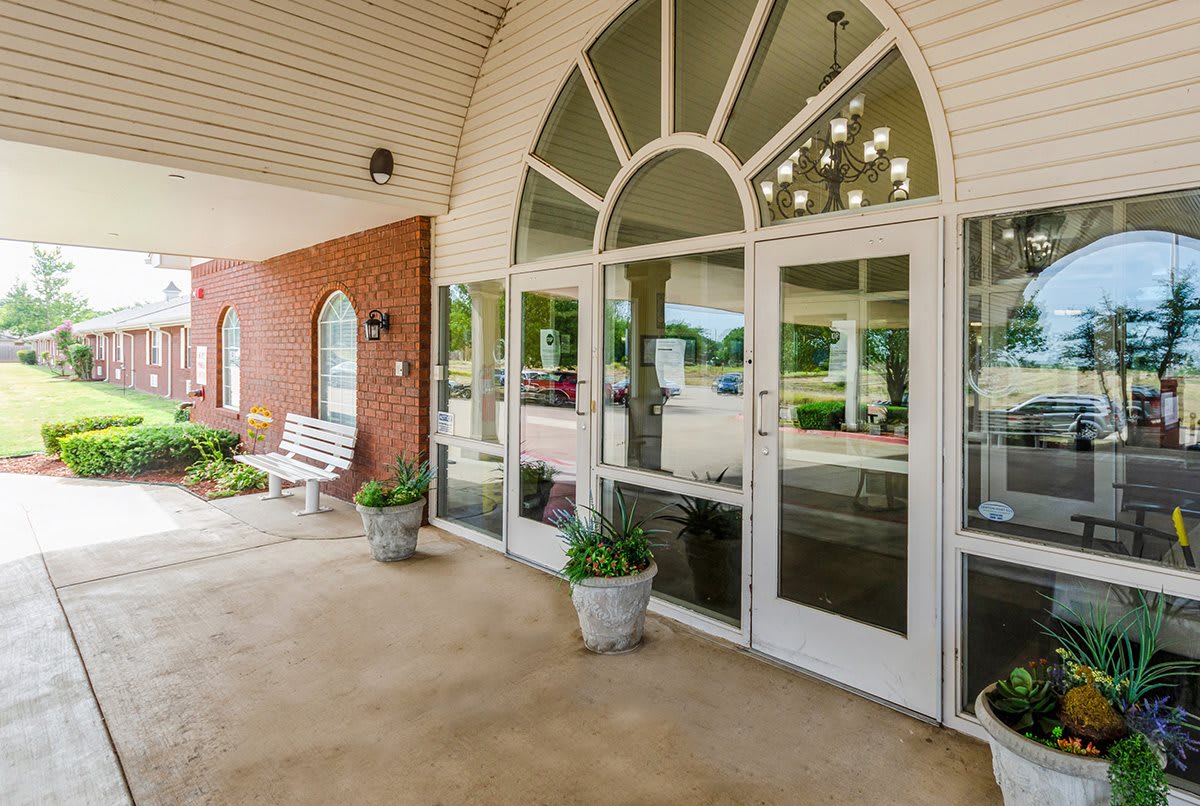 A welcoming entrance to a building featuring large glass doors and decorative planters under a covered porch.