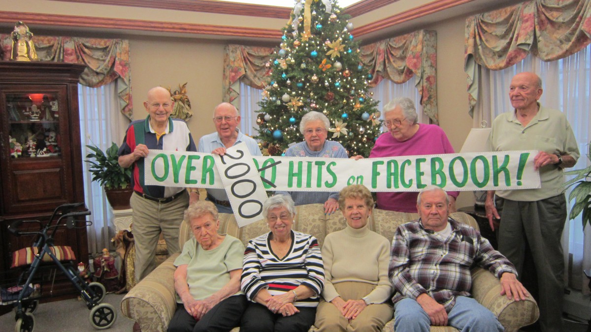A group of elderly people celebrating with a banner in front of a Christmas tree.