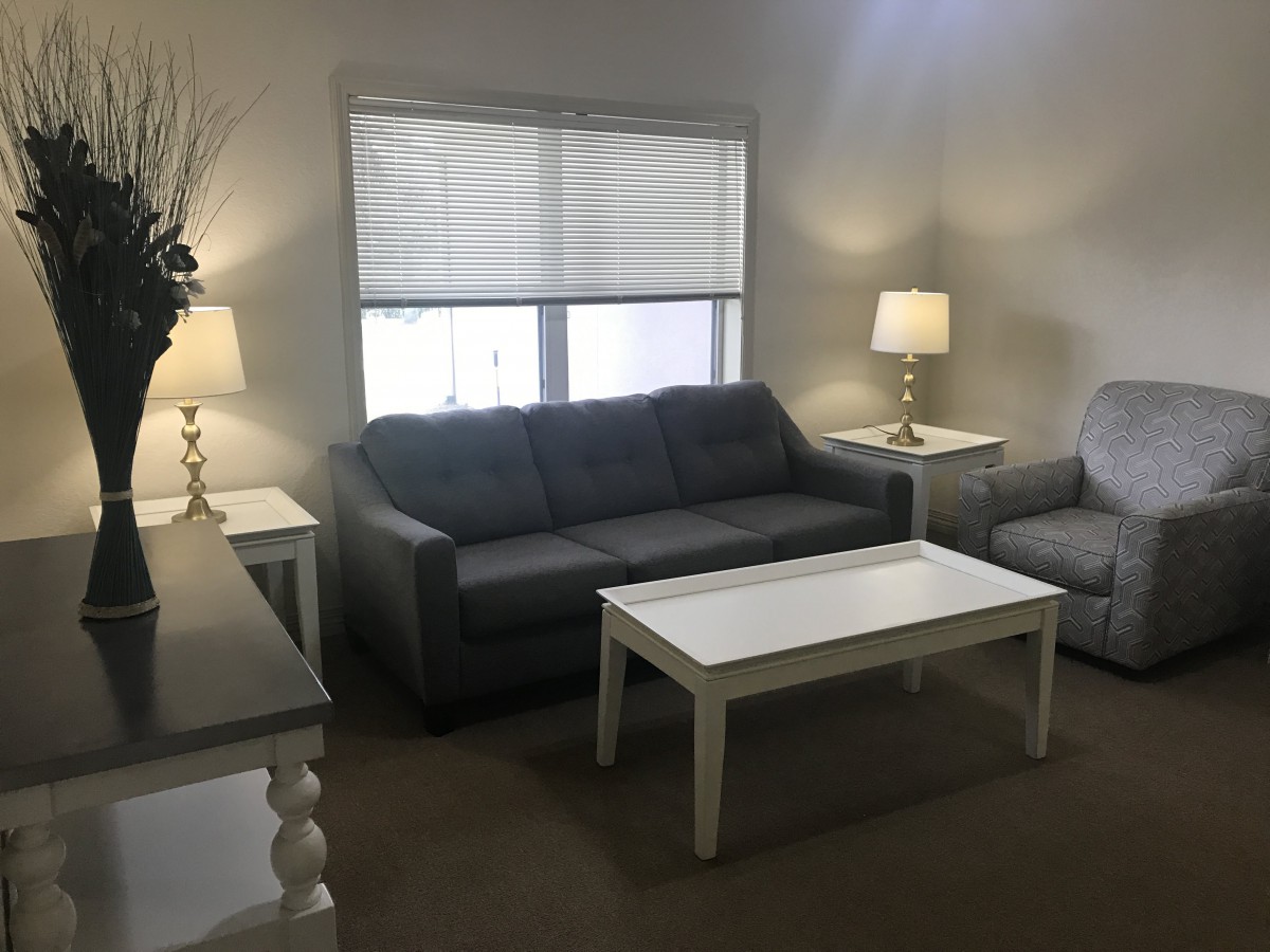 A cozy living room with a sofa, coffee table, and armchair, illuminated by lamps.