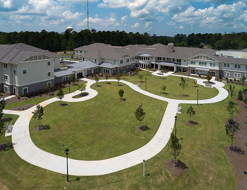An aerial view of a large building complex with winding pathways and surrounding greenery under a partly cloudy sky.