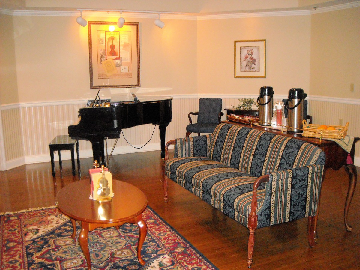 A cozy living room featuring a grand piano, striped sofa, coffee table, and a small refreshment area.