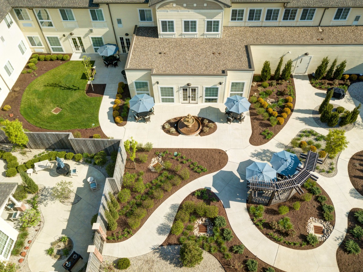 An aerial view of a landscaped residential backyard with winding paths, patios, and garden areas.