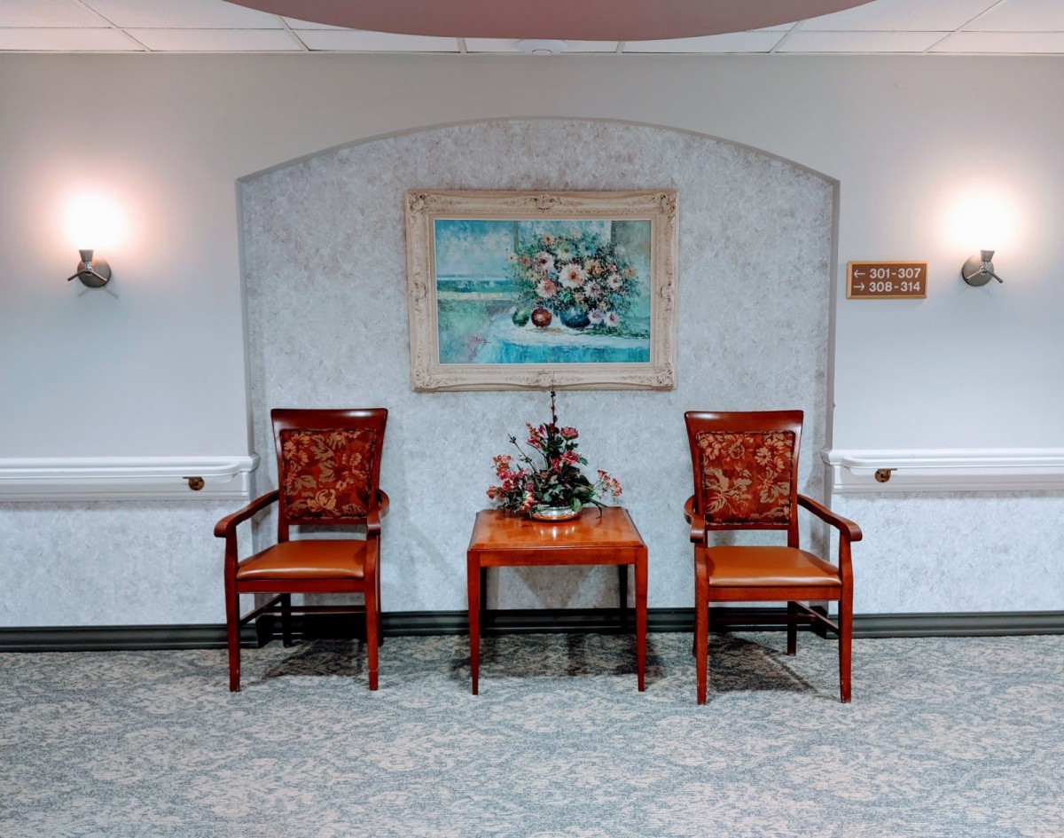 A neatly arranged interior setting featuring two chairs flanking a small table with floral decorations beneath a wall painting.