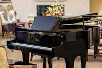 A grand piano positioned in an elegant indoor setting with floral decor in the background.