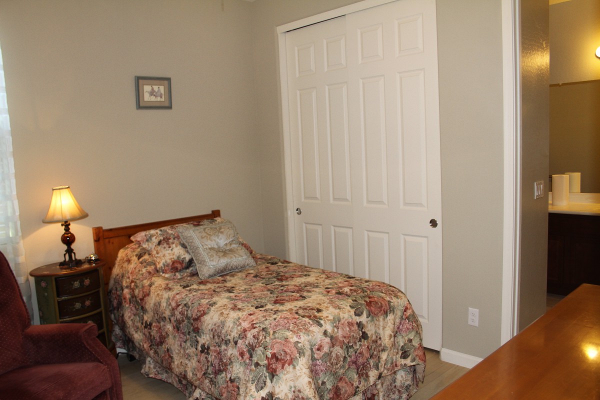 A cozy bedroom with a single bed adorned with floral bedding, featuring a closet and neutral-colored walls.