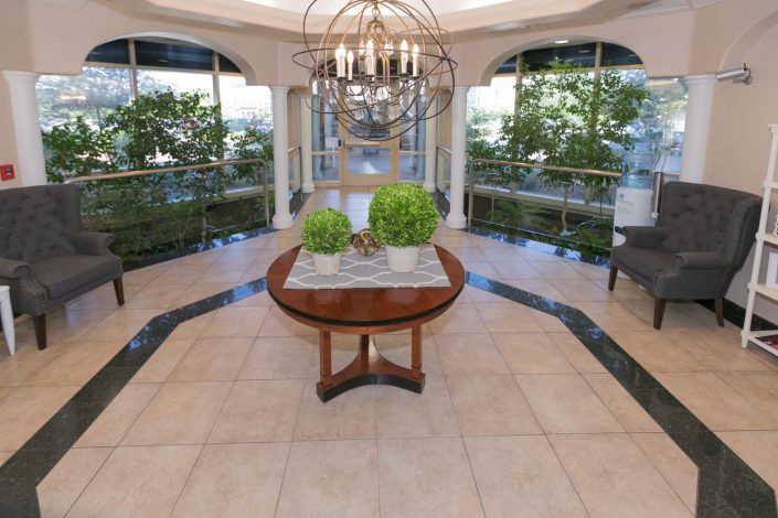Luxurious foyer featuring a central round table with plants, a grand chandelier, and large windows.