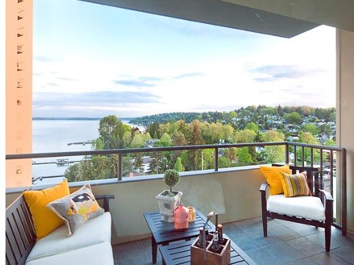 A cozy balcony setup with outdoor furniture overlooking a beautiful lake and lush greenery.