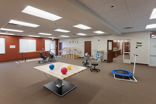 A spacious therapy room equipped with various fitness and rehabilitation tools, including exercise balls, workout machines, and a trampoline.
