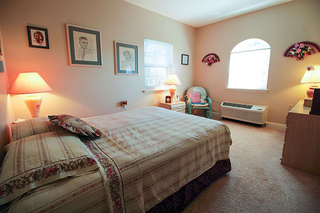 A cozy bedroom with a large bed, bedside lamp, and natural light from windows.