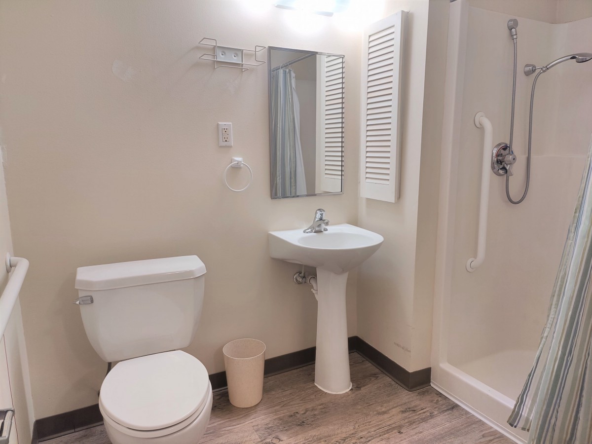 A clean, modern bathroom with a toilet, pedestal sink, mirror, and shower.