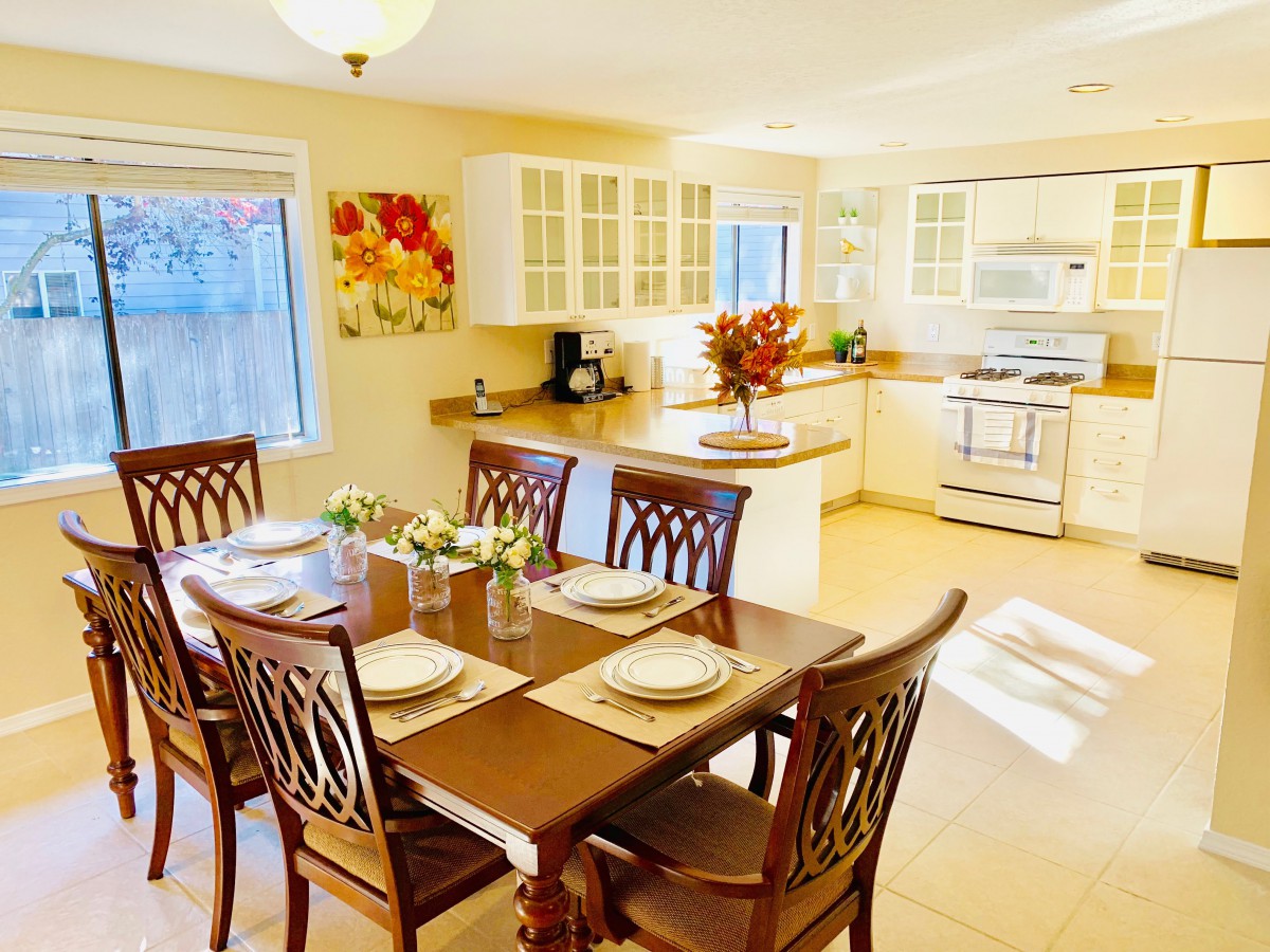A bright, cozy dining room connected to the kitchen features a wooden table set for a meal.