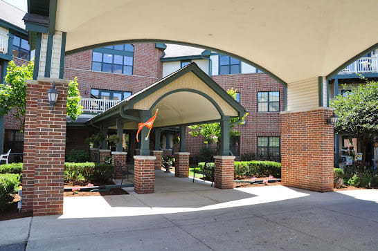 An inviting entrance with an archway leading to a brick building, surrounded by neatly trimmed bushes.