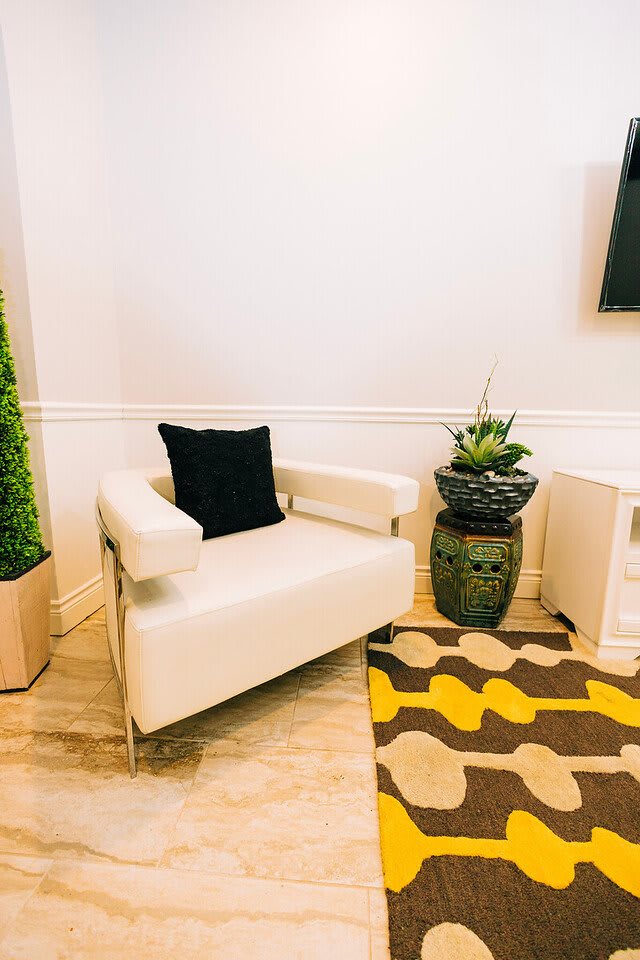 A modern interior with a white chair, decorative plant, and patterned rug.