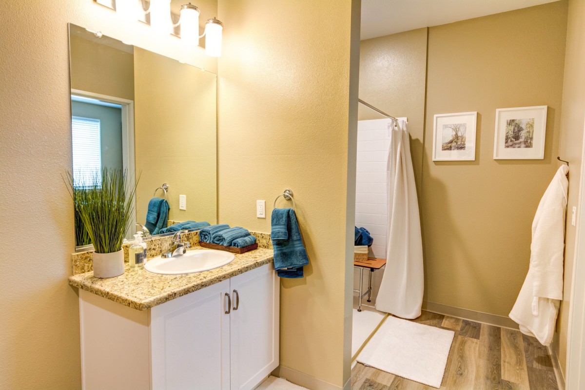 A modern bathroom featuring a sink, mirror, and shower area with teal towels and light decor.