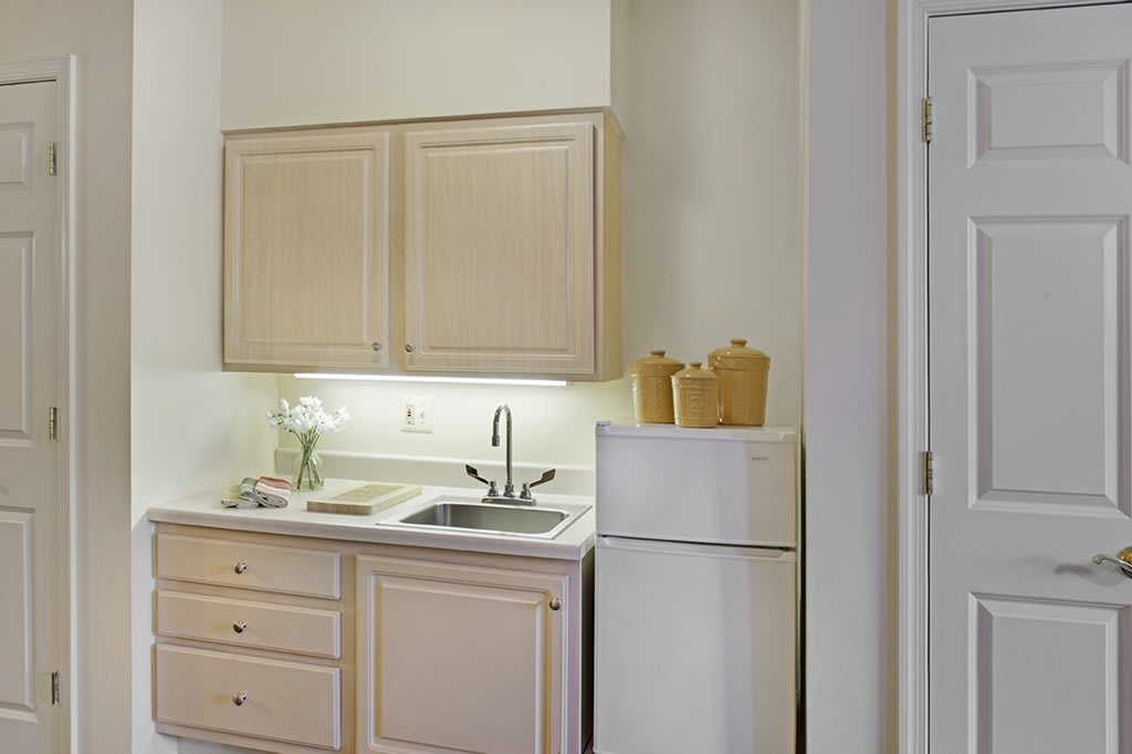 A minimalist kitchen featuring light-colored cabinets, a sink, and a compact refrigerator.