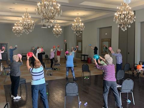A group of seniors participating in an indoor exercise class, using colorful balls for their workout.