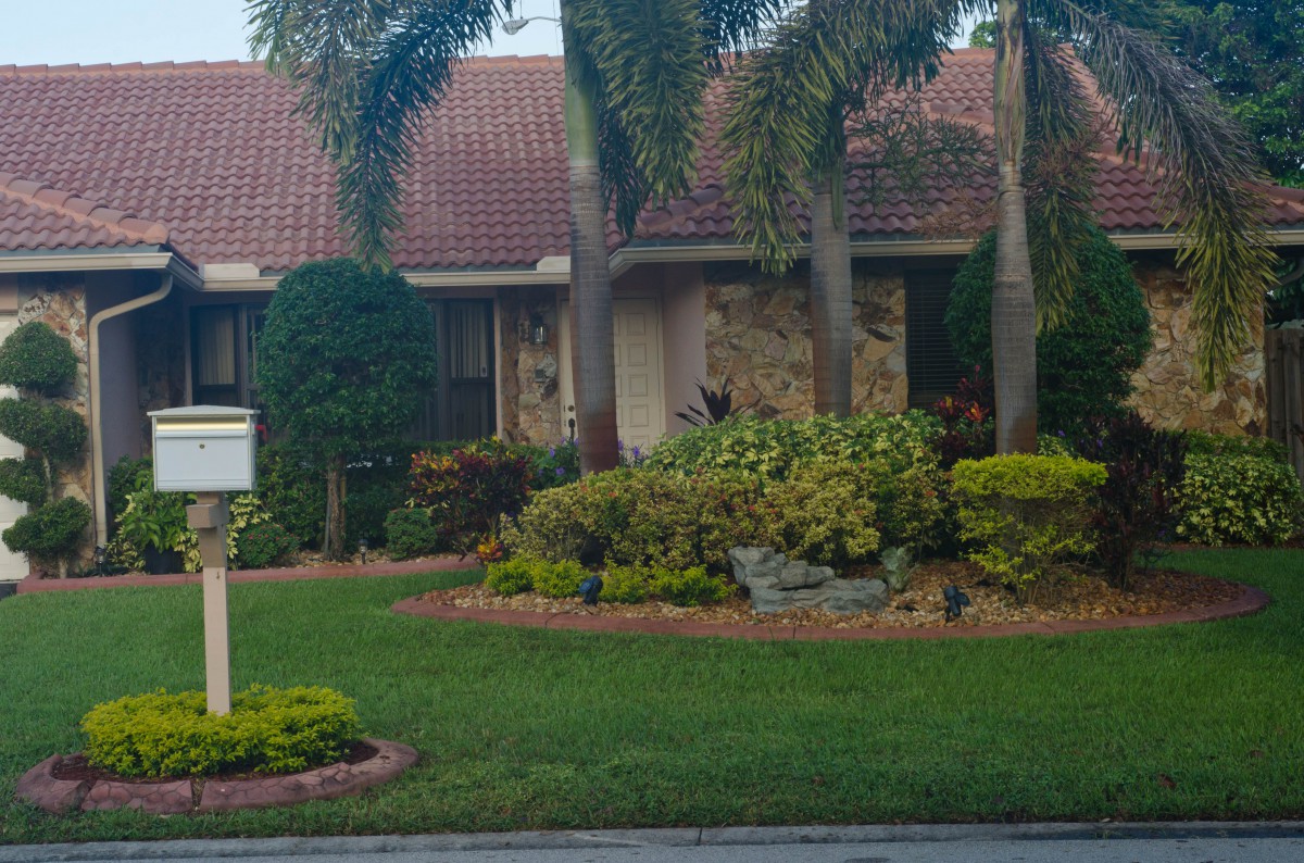 A well-maintained suburban house with a landscaped front yard featuring palm trees and various plants.
