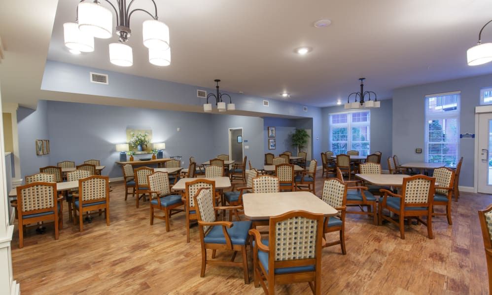 A spacious dining area with wooden tables and chairs, featuring elegant lighting and a wood floor.
