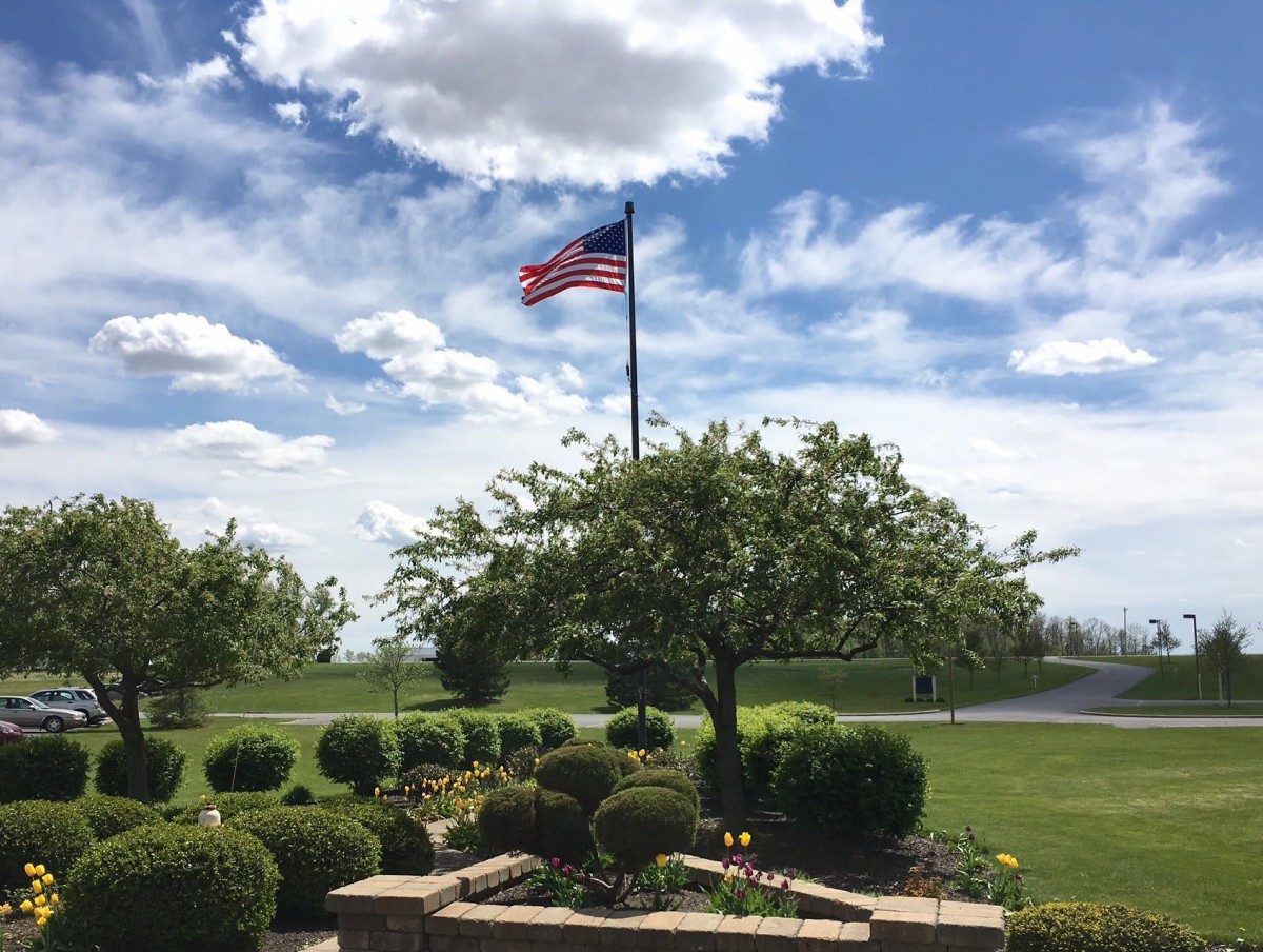 An American flag flies over a beautifully maintained garden with clear skies and scattered clouds.