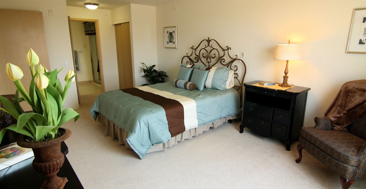 A neatly arranged bedroom with a decorative wrought iron headboard, featuring a bed adorned with blue and brown bedding, flanked by a bedside table with a lamp.