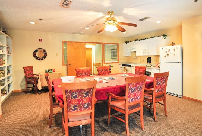 A cozy dining area with a large table, surrounded by chairs and adjacent to a kitchen.