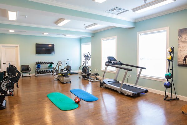 A small home gym with exercise equipment including a treadmill, elliptical, weights, and yoga mats.