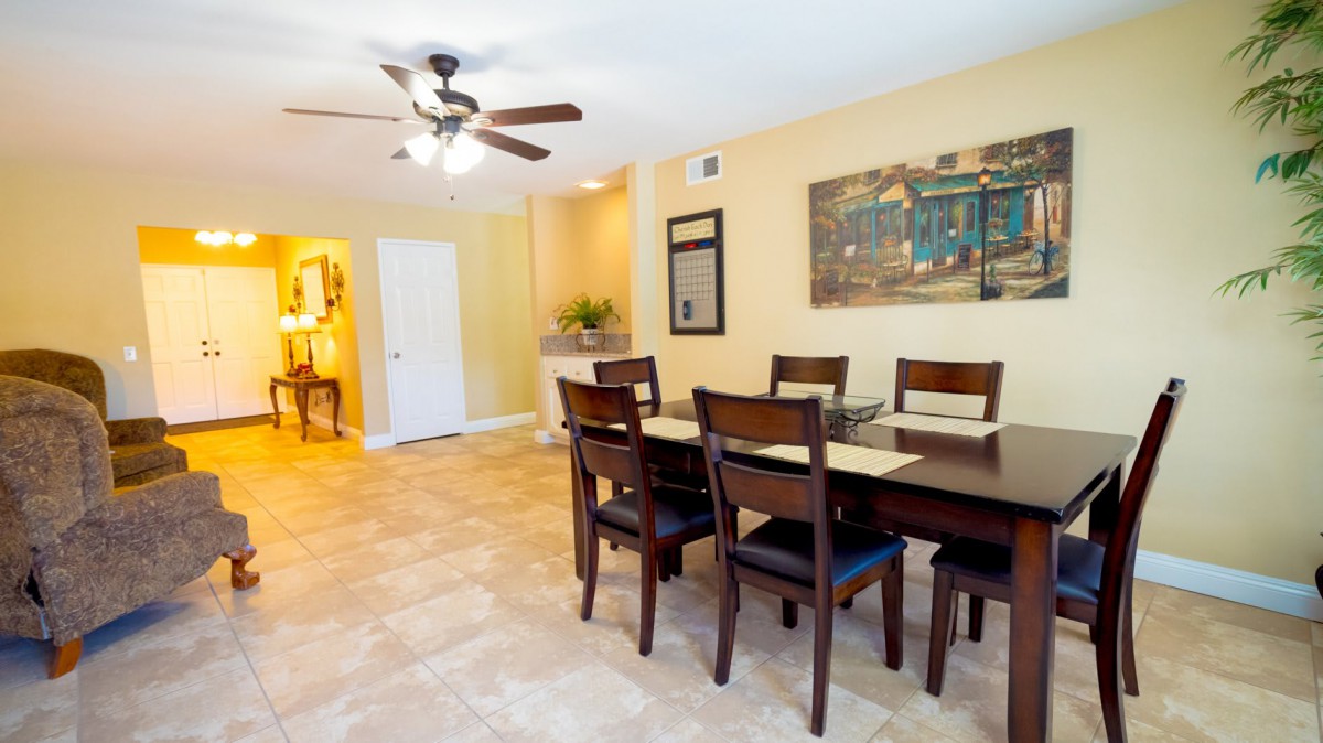 A well-lit dining room with a table, chairs, and ceiling fan.