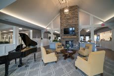 A modern living room featuring a grand piano, cozy seating area, and a stone fireplace under a high vaulted ceiling.