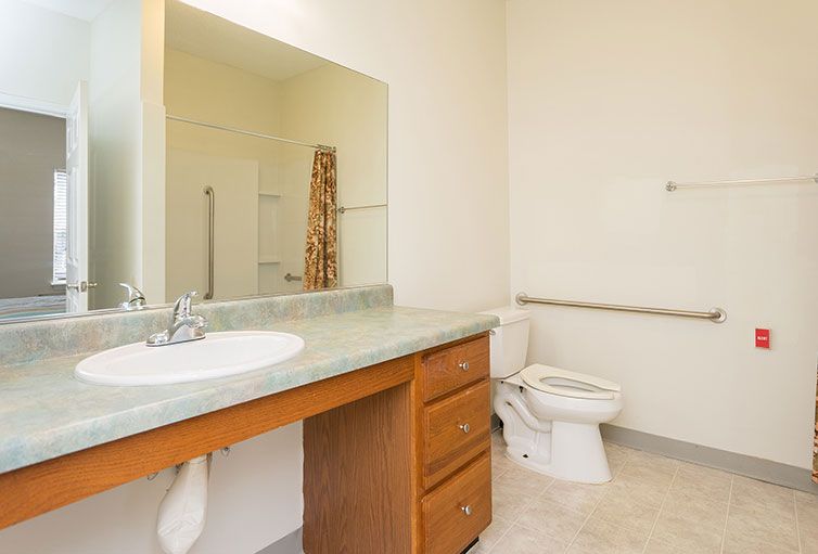A clean and spacious bathroom with a large mirror, sink, and toilet.