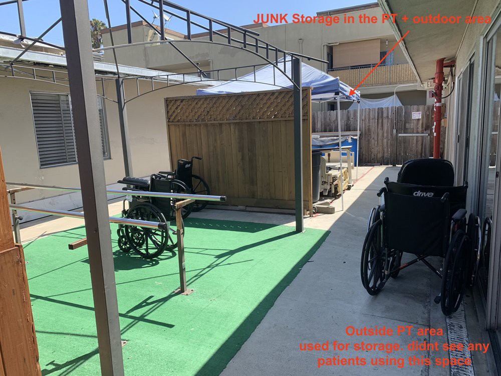 An outdoor pathway with wheelchairs under a shaded area and green carpeting.