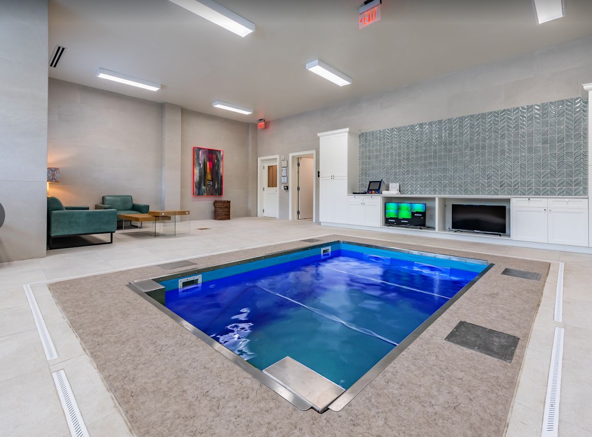 A modern indoor pool with blue lighting, surrounded by a comfortable relaxation area and exercise equipment.