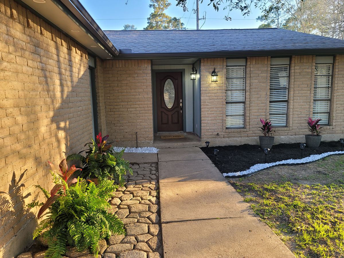 A welcoming entrance of a brick house with a walkway and surrounding plants.