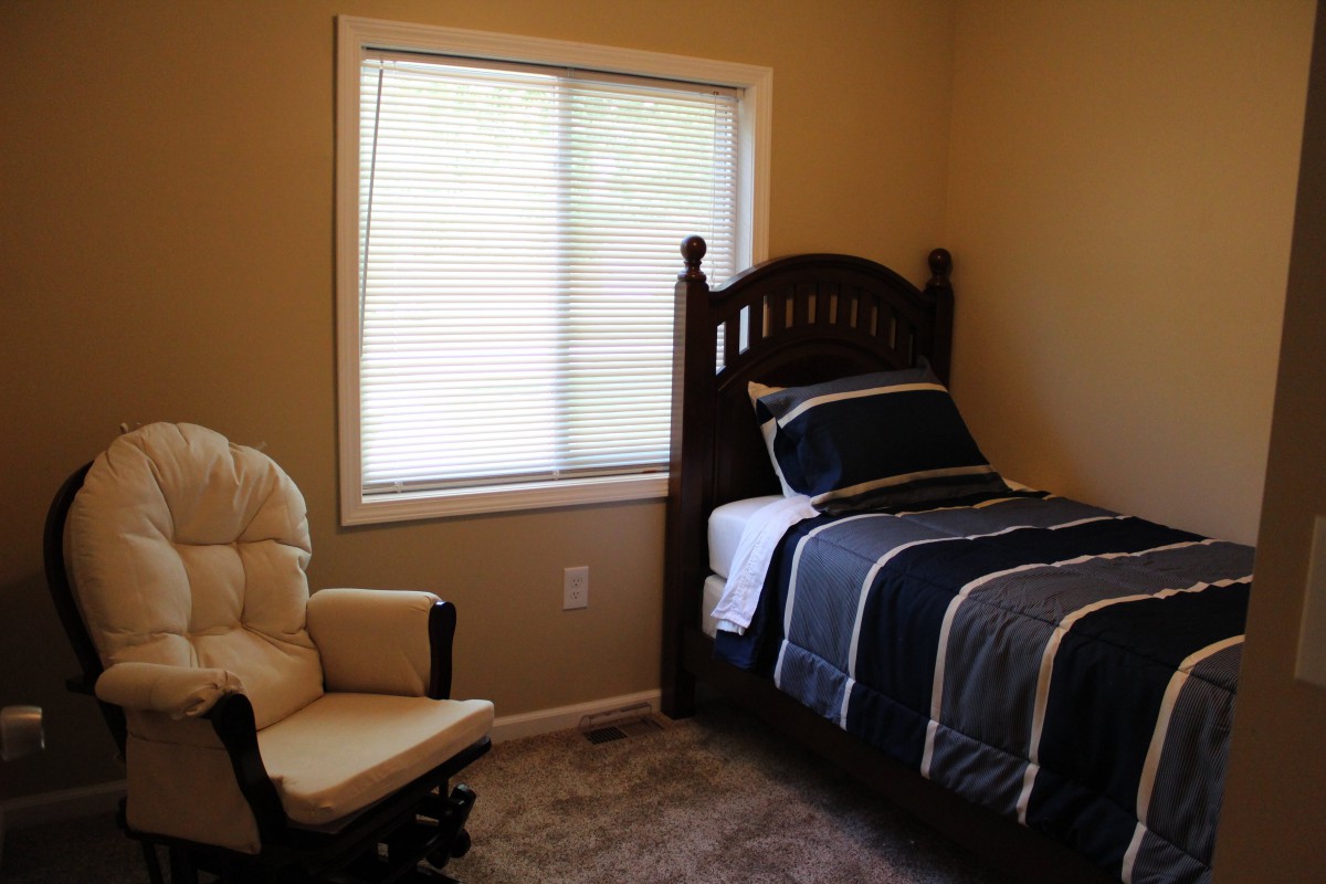 A cozy bedroom with a single bed, rocking chair, and window.