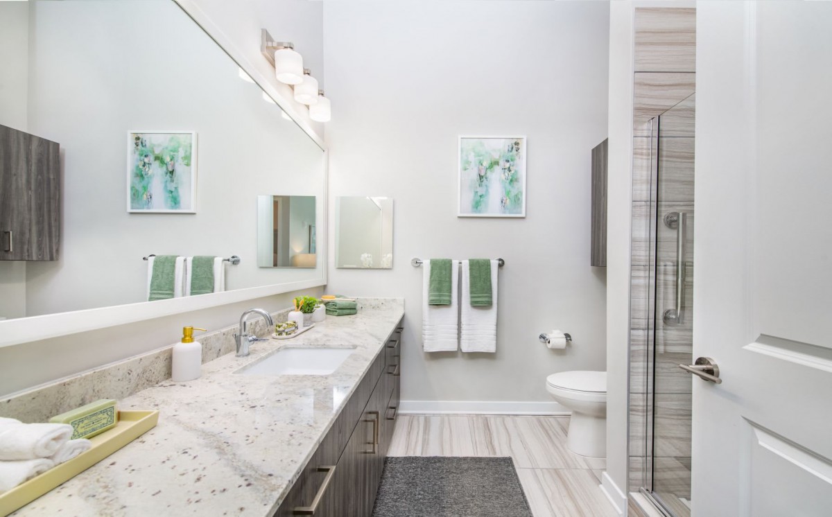 A modern bathroom with a large mirror, marble countertop, and glass-enclosed shower.