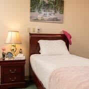 A cozy bedroom with a single bed, nightstand, and a warm lamp.