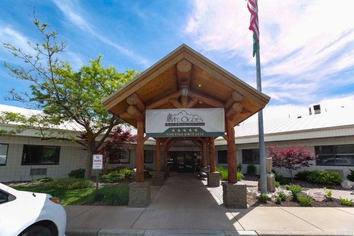 The entrance of a healthcare facility with a wooden canopy and a clear blue sky.