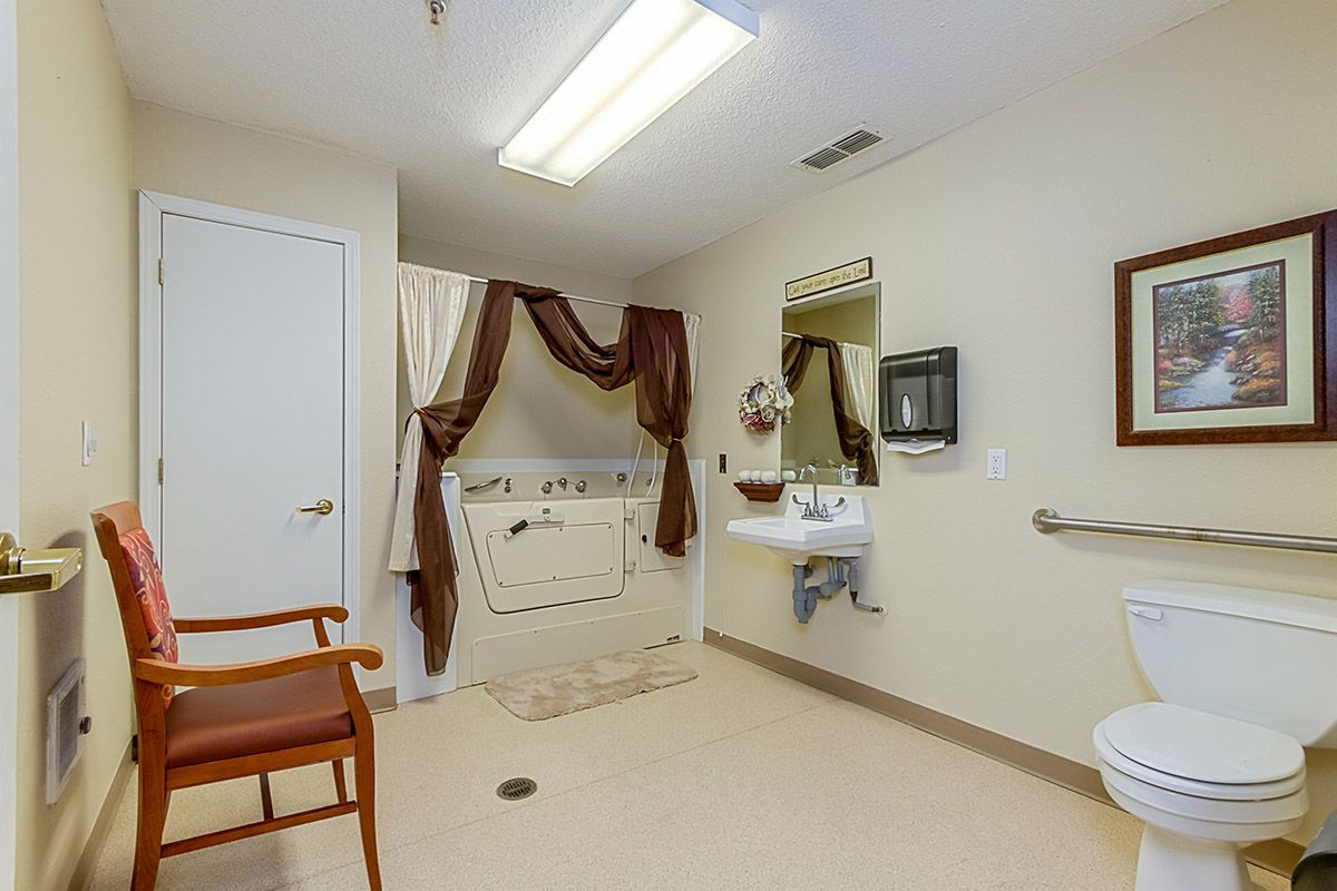 An accessible bathroom with a bathtub, sink, and chair, featuring grab bars for support.
