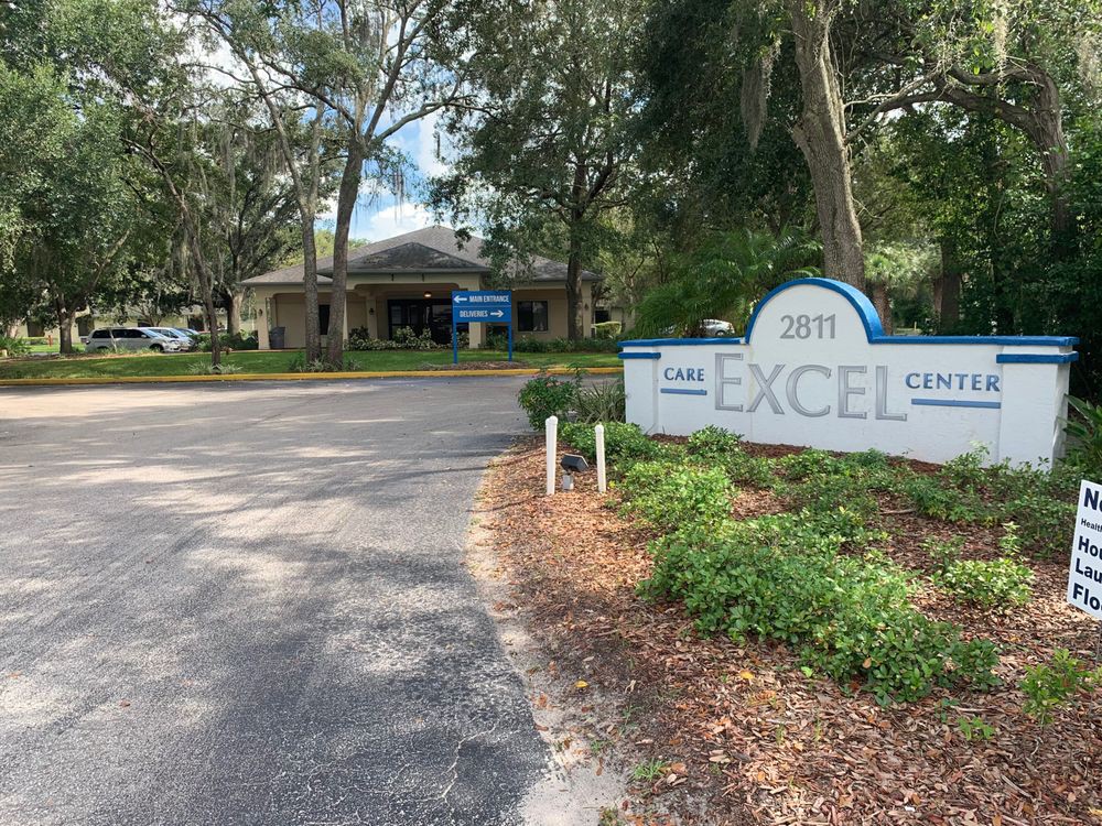 Entrance to a facility with a sign labeled 'EXCEL' amid lush greenery.