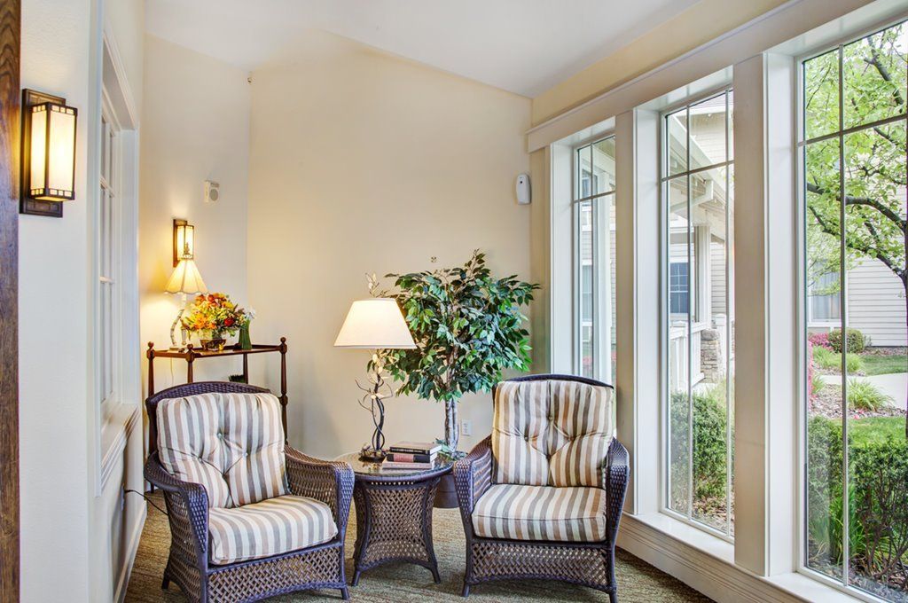 A cozy living room corner with two striped armchairs, a lamp, and large windows.