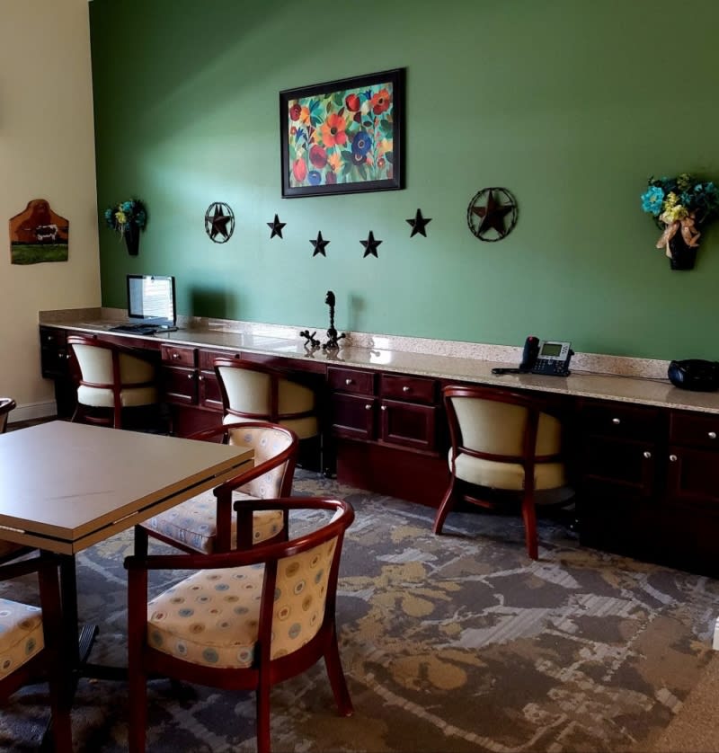 A cozy office workspace with multiple desks, chairs, and a green accent wall featuring decorative artwork.