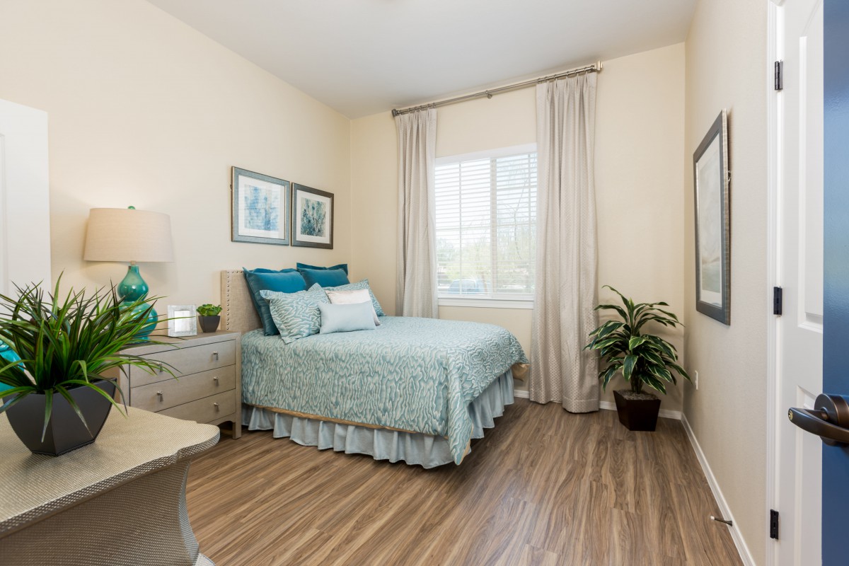 A cozy bedroom with soft lighting, featuring a neatly made bed, wooden flooring, and decorative plants.