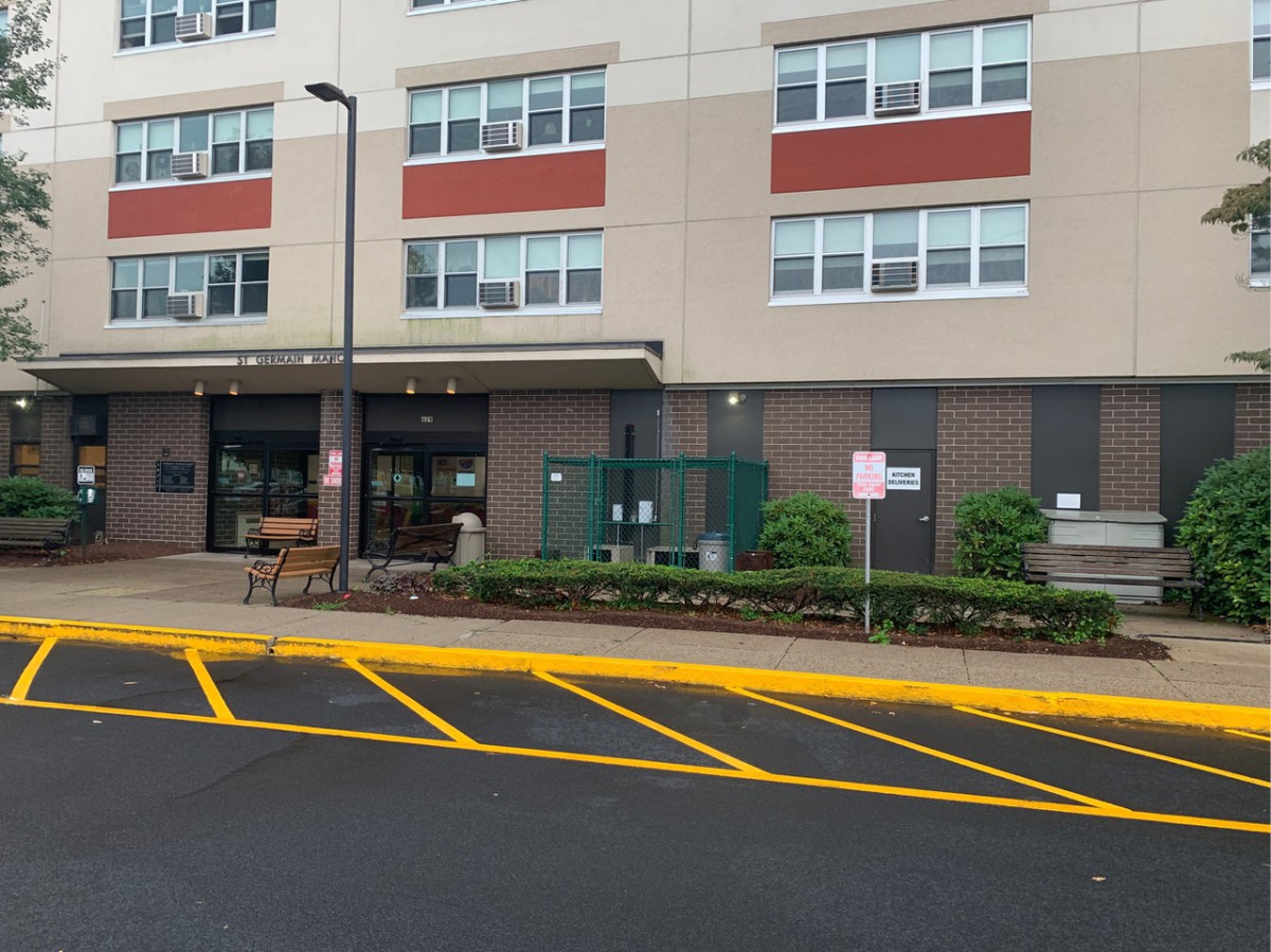 Entrance of a modern apartment building with marked parking spaces.