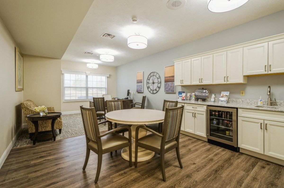 A cozy dining area with a kitchenette featuring round tables and chairs on a wooden floor.